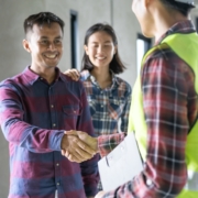 Homeowner shakes hands with a construction professional wearing a safety vest at a residential construction site.