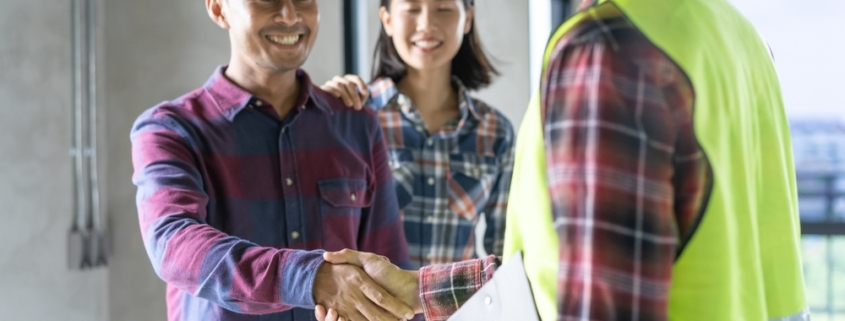 Homeowner shakes hands with a construction professional wearing a safety vest at a residential construction site.