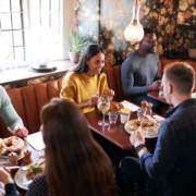 Group of friends enjoying a meal together inside a warmly decorated restaurant with booth seating.